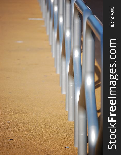 Tram stop railing with metal guards reflecting the blue sky and orange gravel