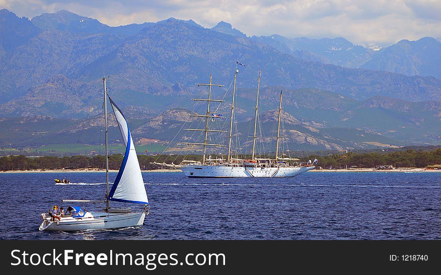 A sailboat passing in front of a clipper tall ship in the bay of Calvi. A sailboat passing in front of a clipper tall ship in the bay of Calvi