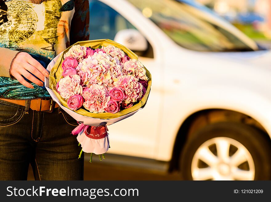 Hands of young unidentified woman holding a beautiful bouquet of pink peonies flowers wrapped in paper outdoors