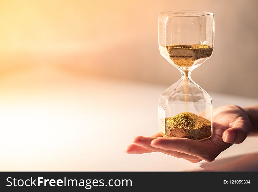 Close up of brown sand running through the shape of modern hourglass on male hand.Time passing and running out of time. Urgency countdown timer for business deadline concept with copy space. Close up of brown sand running through the shape of modern hourglass on male hand.Time passing and running out of time. Urgency countdown timer for business deadline concept with copy space