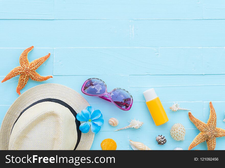 Beach accessories including sunglasses, starfish, hat beach, sunblock, colorful flip flop and shell on bright blue pastel wooden background for summer holiday and vacation concept.