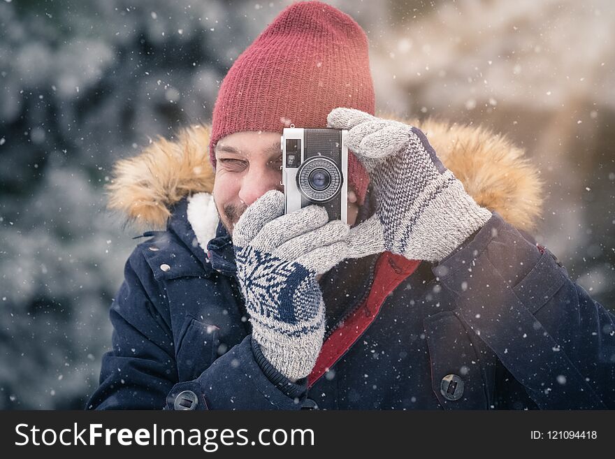 Fashionable Man Taking Pictures With Retro Camera On Snowy Day. Winter Vacation Travel Concept.