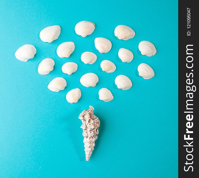 Seashell of cone shape with many little seashells on blue paper background. Summer composition in minimal style. Flat lay, copy space, top view