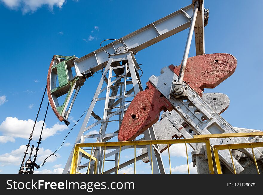 Oil and gas industry. Work of oil pump jack on a oil field. White clouds and blue sky. oil well pump. Oil and gas industry. Work of oil pump jack on a oil field.