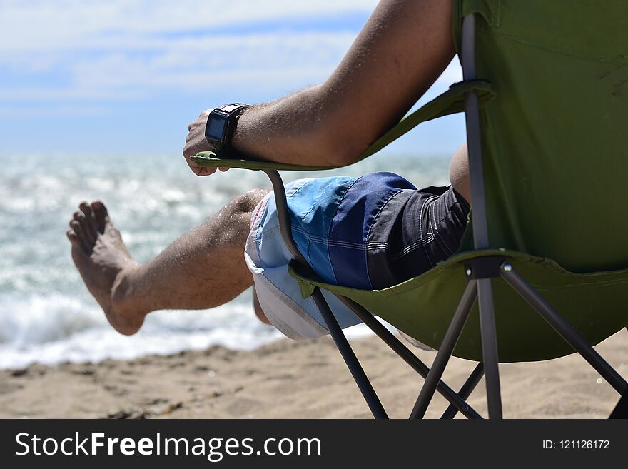 Man resting sitting on a chair and enjoys lifting his legs and enjoying the sea breeze. Man resting sitting on a chair and enjoys lifting his legs and enjoying the sea breeze