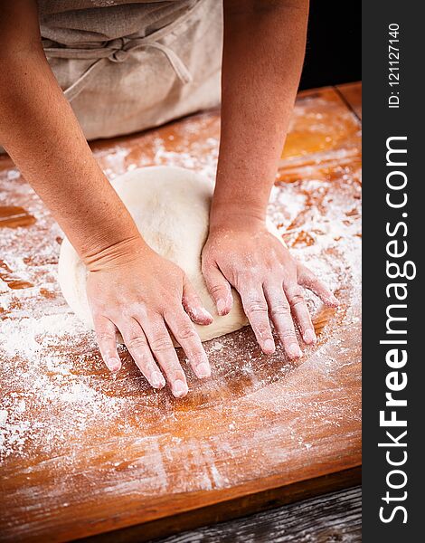 Woman`s hands knead dough on a table