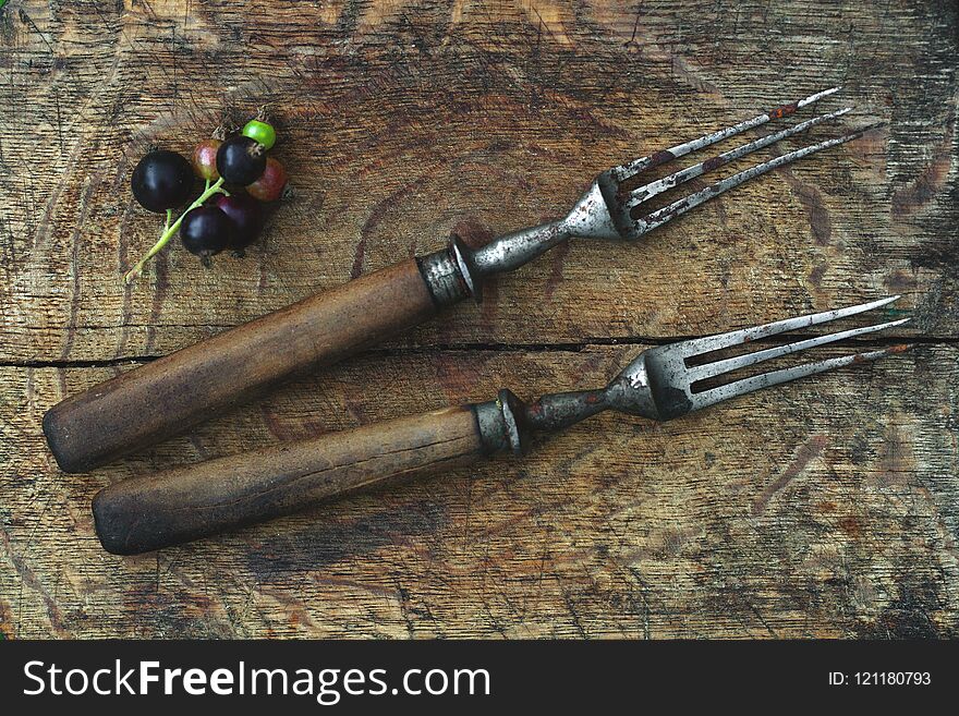 Ancient forks on a wooden board, a branch of black currant. Close-up, top view
