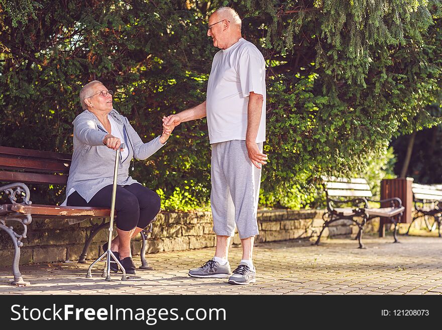 Aging senior man supporting ill wife in the park