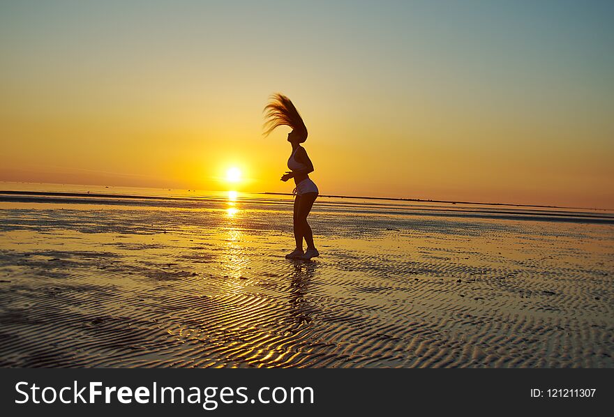 Silhouette flexible gymnastics girl on the shore of Sea during twilight.