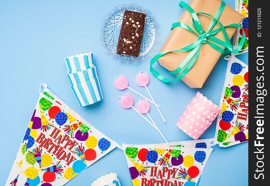 Happy Birthday party items flat lay. Candles, gift box, decoration banner, paper glasses, chocolate cake