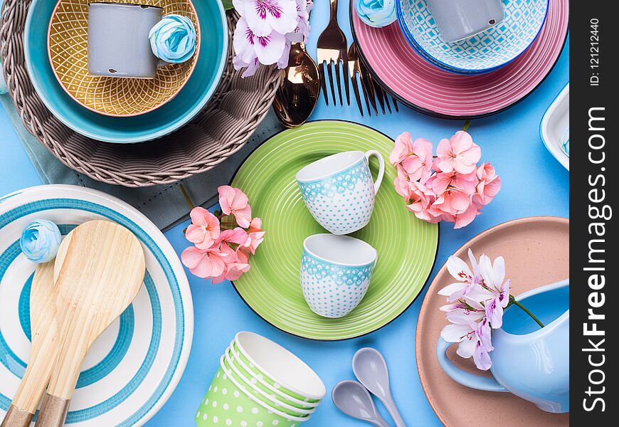 Tableware dish set on blue pastel background with flowers. Flat lay