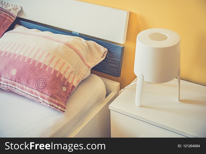 White lamp on night table next to the bed in modern hotel bedroom. Cozy living concept. Close up. White lamp on night table next to the bed in modern hotel bedroom. Cozy living concept. Close up.