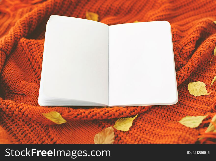 A notebook with autumn leaves on reddish knittted background. Mock up, place for your text.