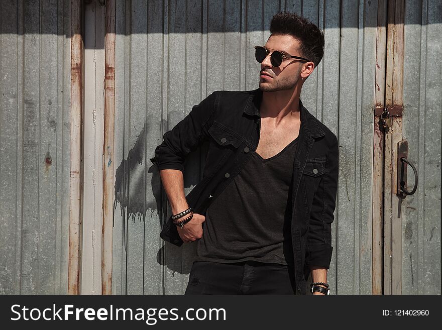 Casual man standing on metal wall background looks to side while wearing black shirt and sunglasses, portrait picture
