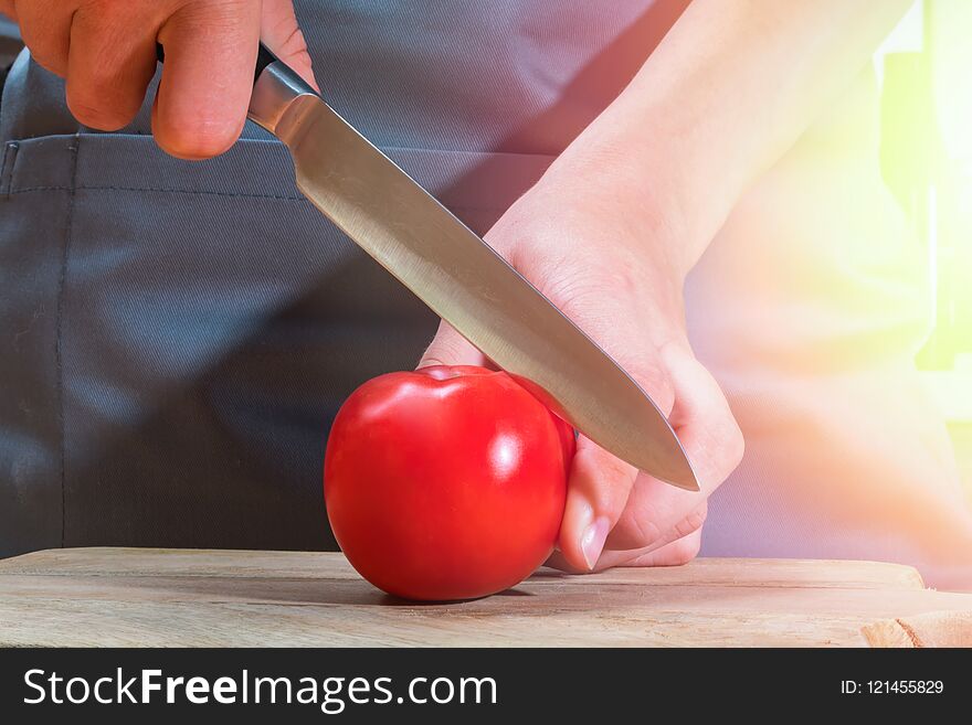 Female hands with knife cutting ripe red tomato on wooden board. Warm sunny patch of light.