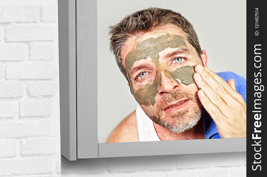Lifestyle mirror portrait of young attractive and happy man with bathroom towel with green cream on his face applying facial mask in skin care beauty and male cosmetics use concept