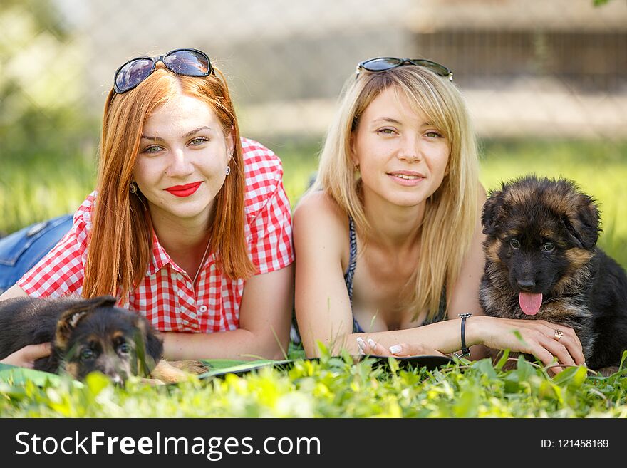 Two young smiling women lying on grass with small puppies of german shepherd. Two young smiling women lying on grass with small puppies of german shepherd