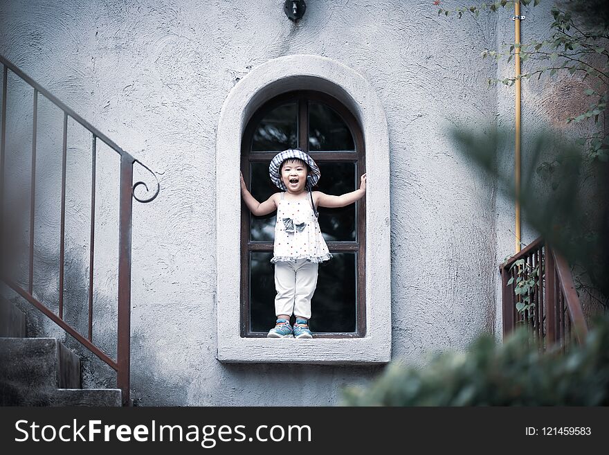 Happy cute little girl smiling and standing by the window