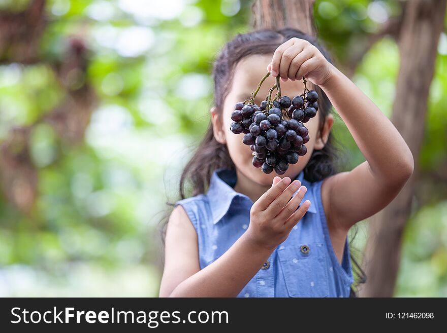 Cute asian child girl holding bunch of red grapes