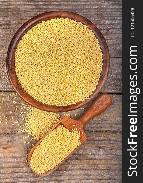 Millet in brown wooden bowl on wooden table with the spoon. Spilled millet.