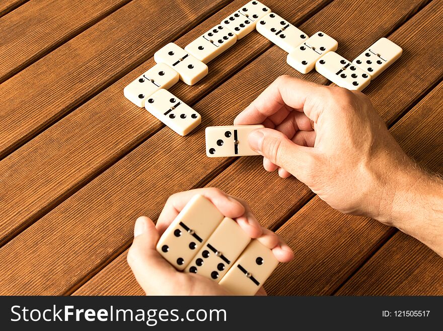 Playing dominoes on a wooden table. Man`s hand with dominoes