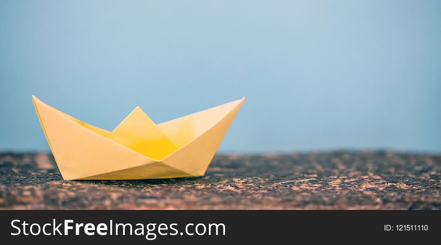 Yellow paper folded, origami, boat on a rock, blue background, copy space. Yellow paper folded, origami, boat on a rock, blue background, copy space