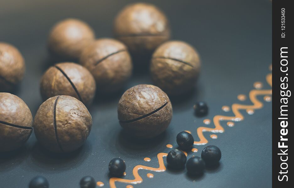 macadamia, Australian nut and juniper berries in a ceramic plate on a wooden table, close-up, toned. macadamia, Australian nut and juniper berries in a ceramic plate on a wooden table, close-up, toned