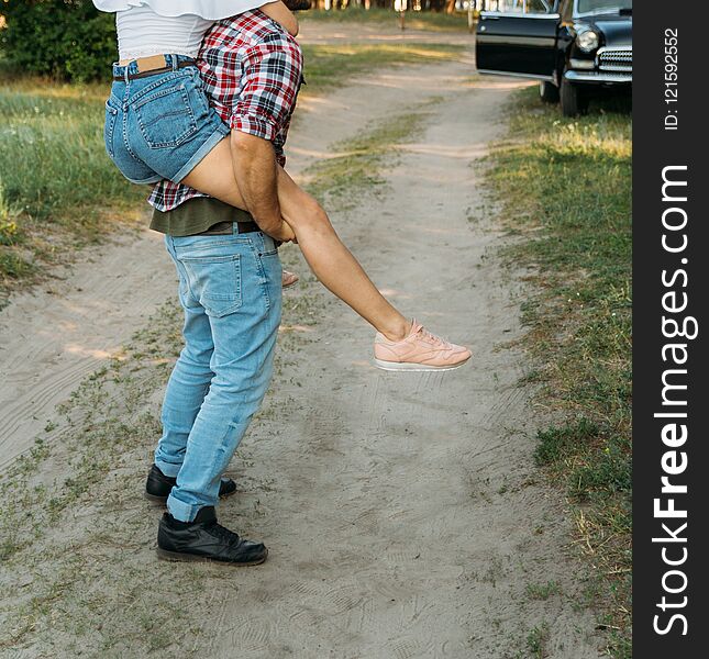 The Girl Jumped On The Guy`s Back.he Holds Her Legs. Check Shirt And Jeans.in The Background Is A Black Car In The Forest