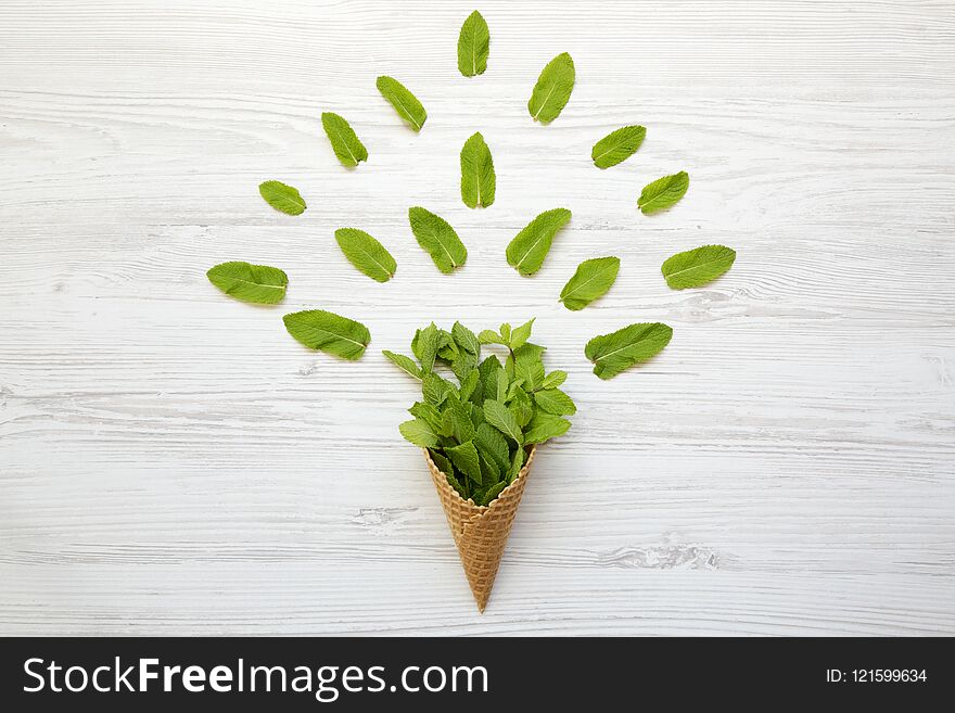 Waffle sweet cone with mint leaves over white wooden surface, top view. Flat lay, overhead. Summer background.