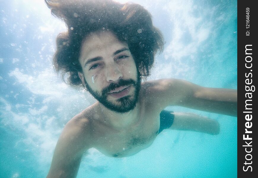 Attractive young man submerged in pool looking at camera