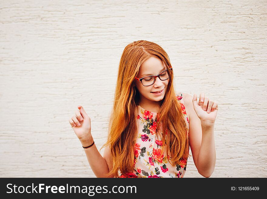 Portrait of adorable preteen kid girl of 10-11 yers old with long red hair, wearing eyeglasses