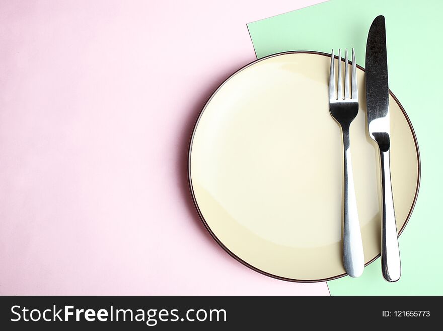 Plate, fork and knife on a pink and green background. Concept table setting. Top view