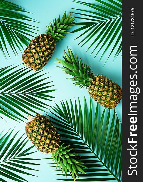 Pineapples and tropical palm leaves on pastel turquoise background. Summer concept. Creative flat alay with copy space
