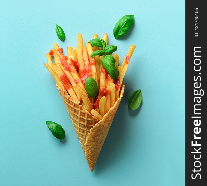 Fried potatoes in waffle cones on blue background. Hot salty french fries with tomato sauce, basil leaves. Fast food