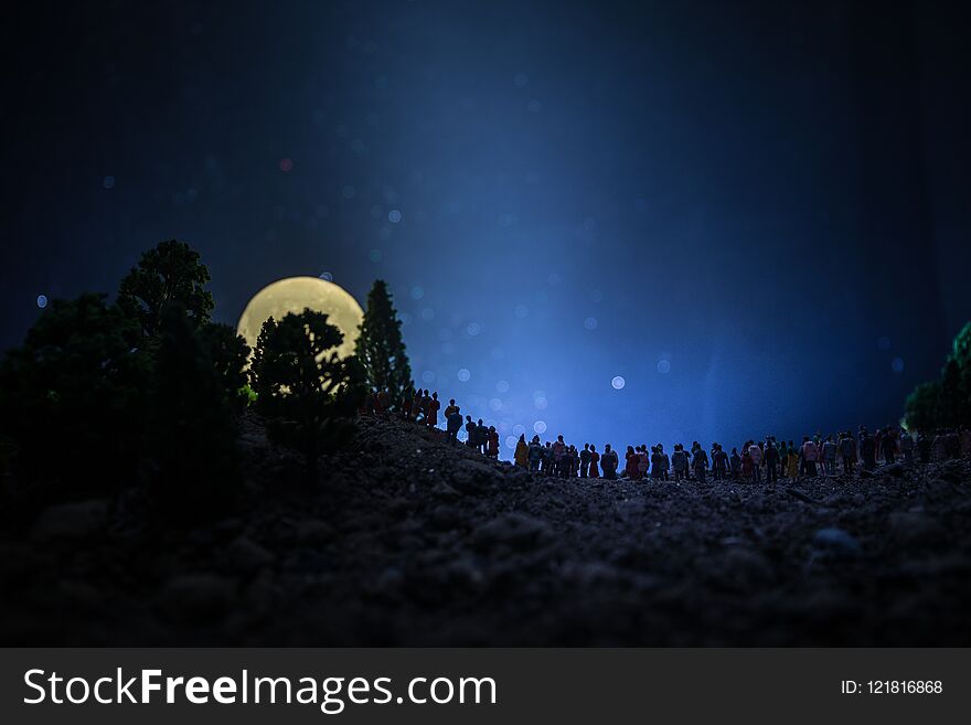 Silhouette of a large crowd of people in forest at night watching at rising big full Moon. Decorated background with night sky wit