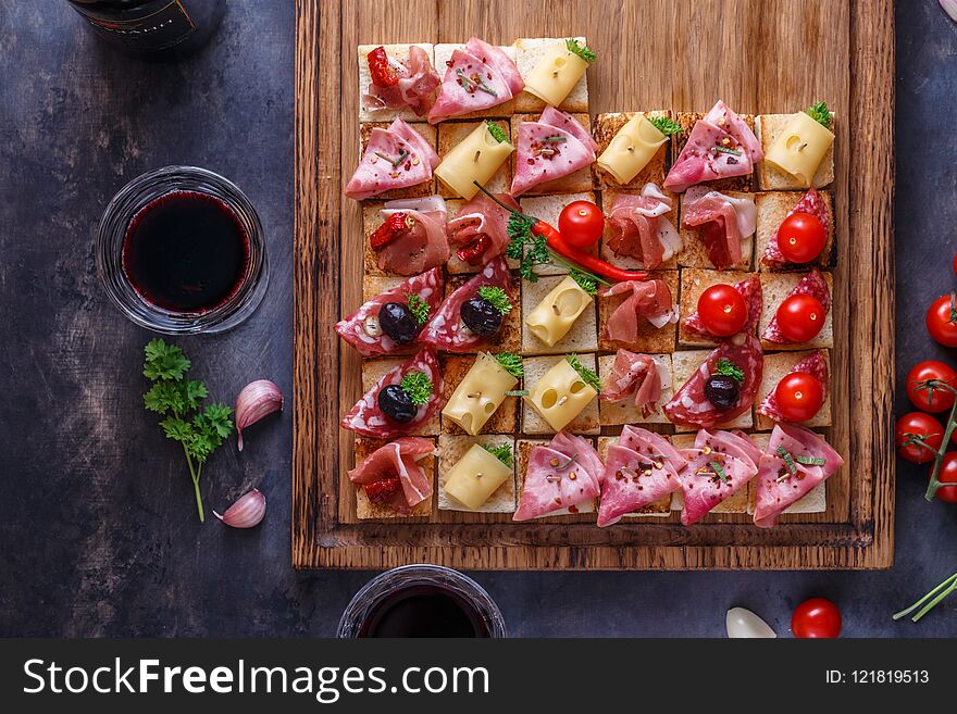 Tasty savory tomato Italian appetizers, or bruschetta, slices of toasted baguette topped with ham, prosciutto on a wooden board.