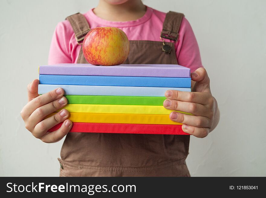 The schoolgirl is holding books and an apple. Hands of the child. Back to school. Life style. A girl in a pink T-shirt is going to learn.