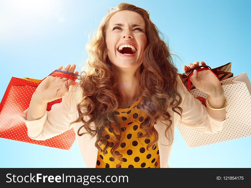 Happy modern woman in a light jacket with shopping bags rejoicing against blue sky. Happy modern woman in a light jacket with shopping bags rejoicing against blue sky