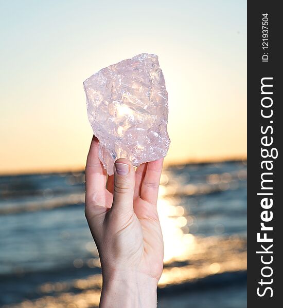 Woman`s hand holding gem grade rough Rose Quartz chunk from Madagascar in front of the lake at sunrise