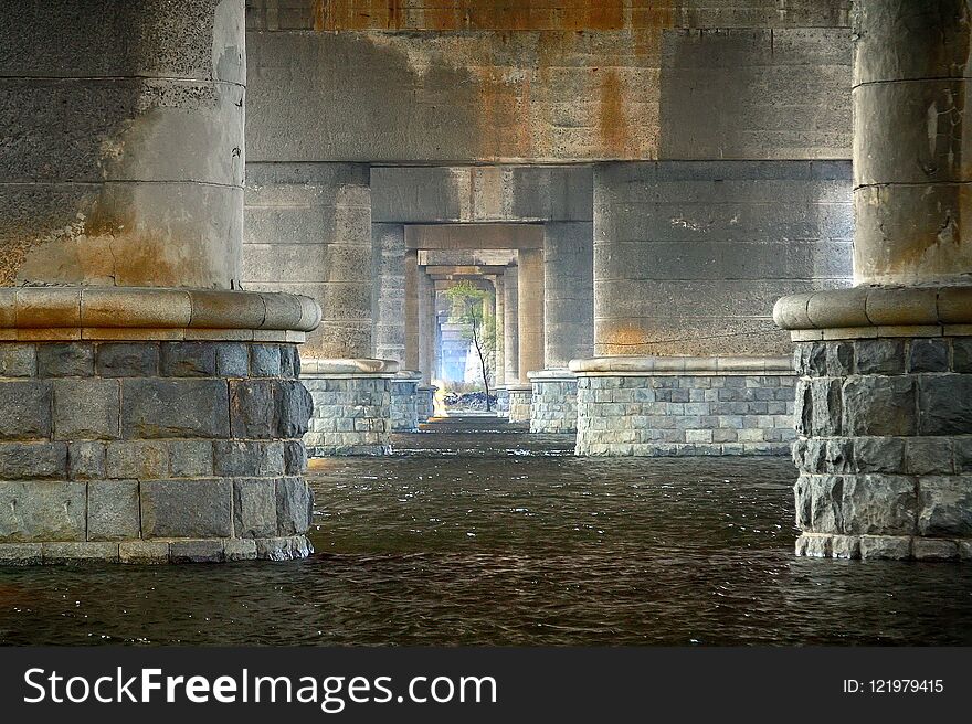 The view under the bridge. The river flows between the stone supports of the bridge. The view under the bridge. The river flows between the stone supports of the bridge