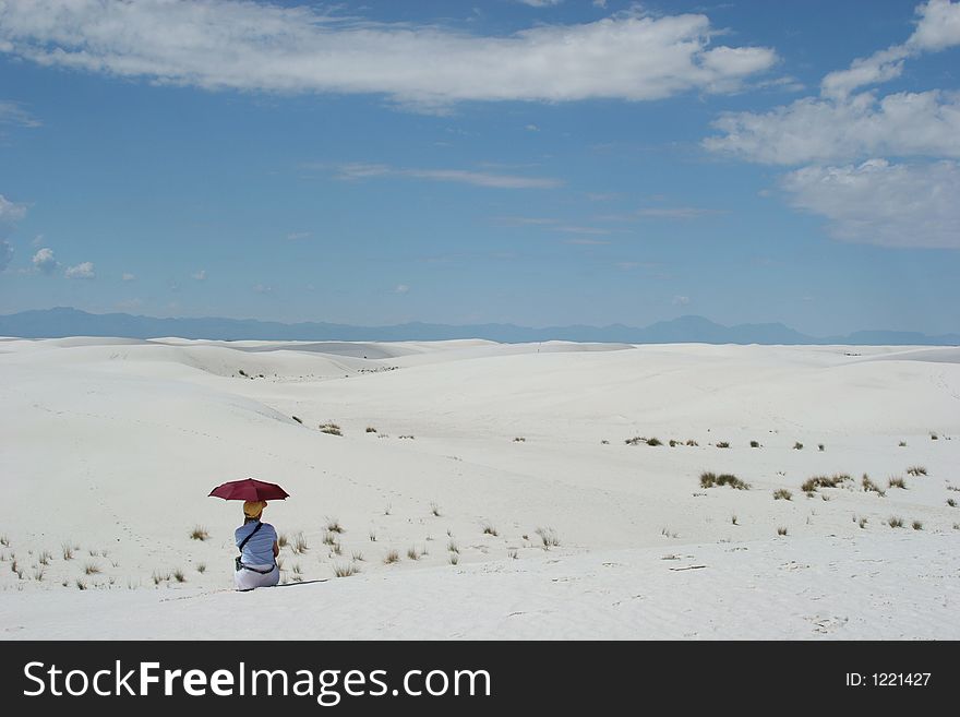 Woman sitting on white sand dunes holding an umbrella. Woman sitting on white sand dunes holding an umbrella