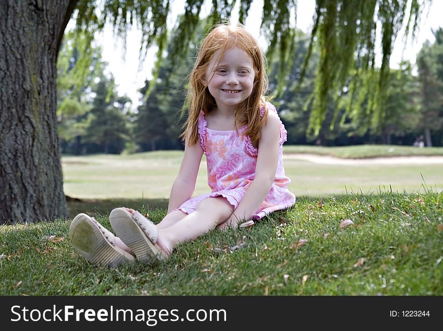 Small redhaired girl sitting under a willow tree in summertime. Small redhaired girl sitting under a willow tree in summertime.