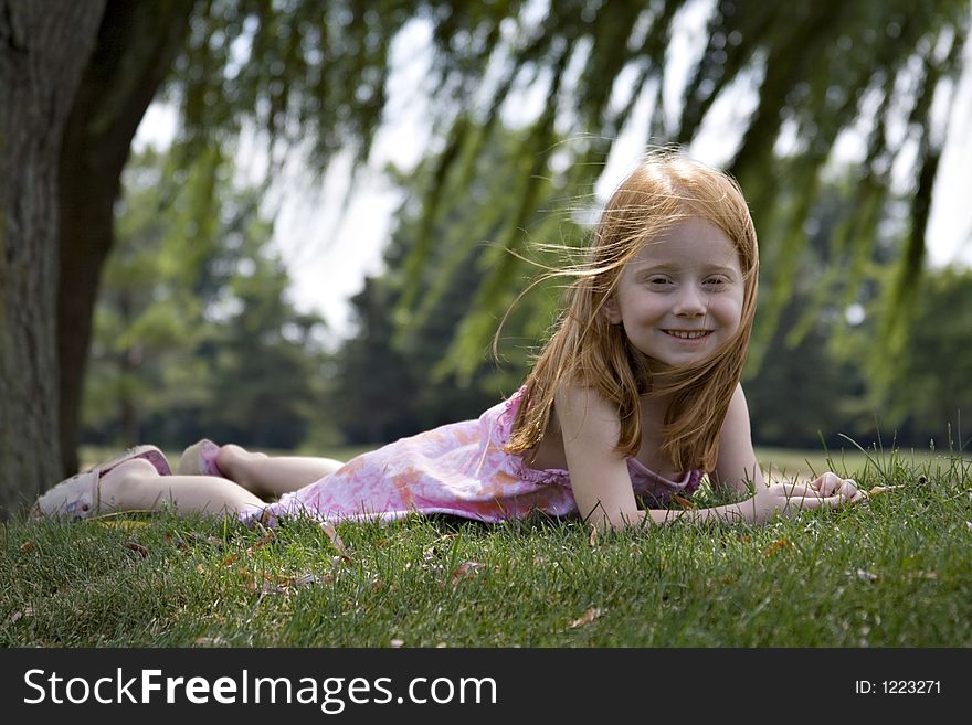 Small red-haired girl laying in the grass under willow trees. Small red-haired girl laying in the grass under willow trees.