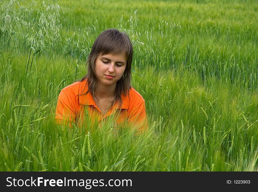 Photo of girl in orange shirt sitting in green wheat field. Photo of girl in orange shirt sitting in green wheat field