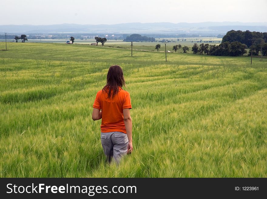 Photo girl in orange shirt walking in green wheat field looking out over wide valley. Photo girl in orange shirt walking in green wheat field looking out over wide valley