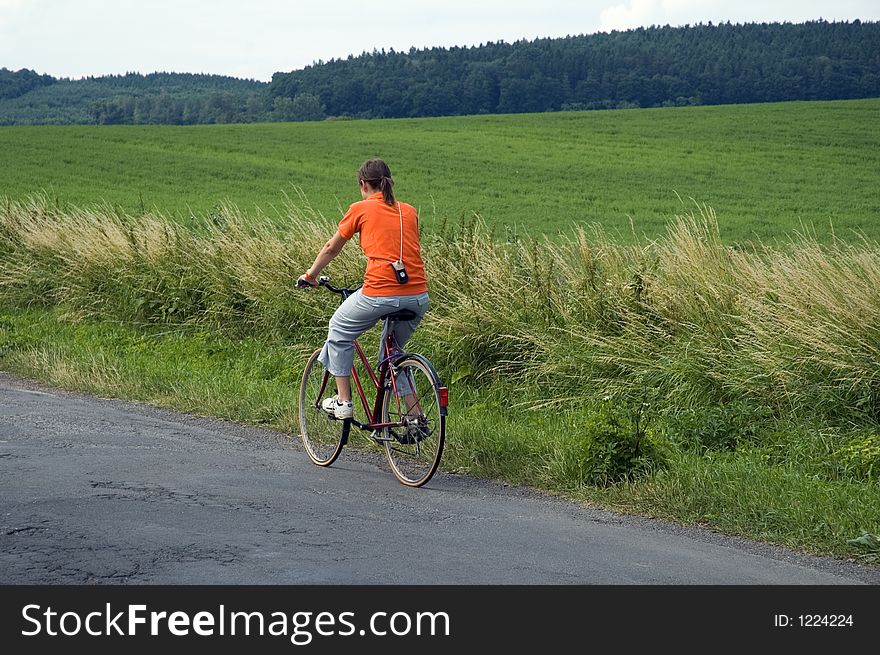 Girl in orange riding bicycle in country field. Girl in orange riding bicycle in country field