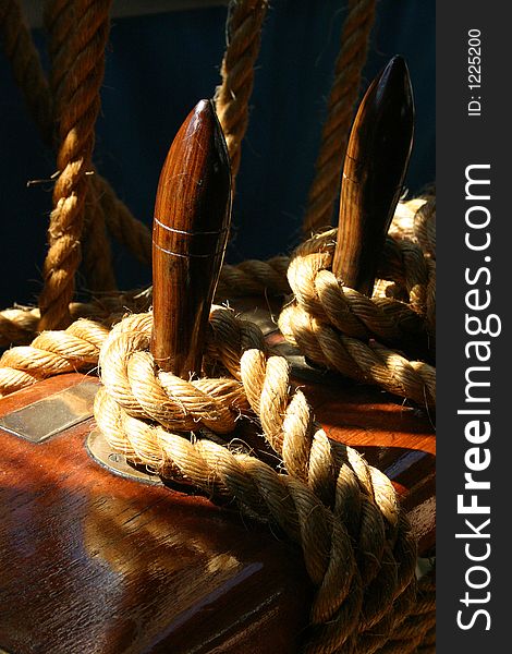 Natural rope tied around polished wodden cleat photographed on dark background. Natural rope tied around polished wodden cleat photographed on dark background