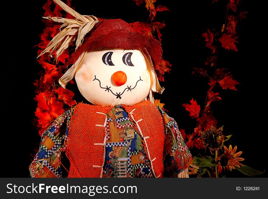 A Halloween Scarecrow or autumn scarecrow among autumn leaves and sunflowers.