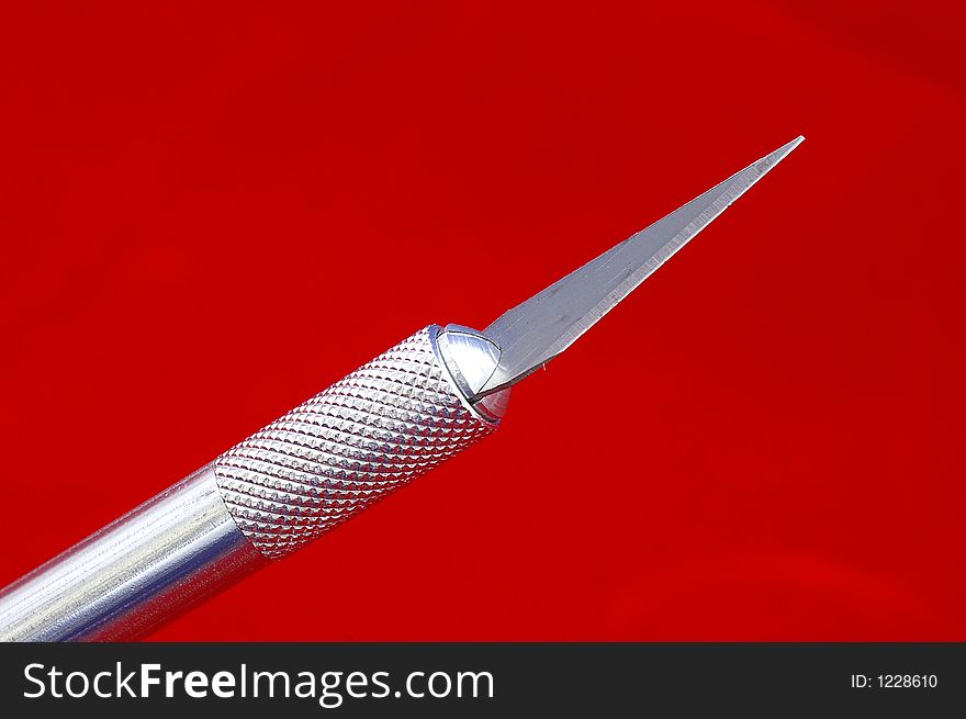 Closeup of a hobby knife blade against a bright red background. Closeup of a hobby knife blade against a bright red background