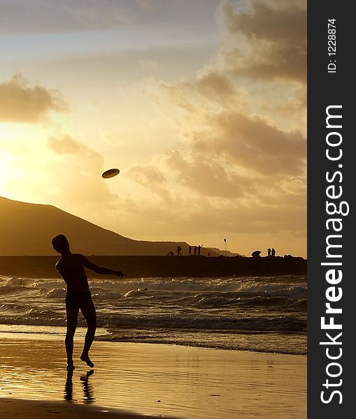 A man throws a frisbee in the ocean on an beach at sunset